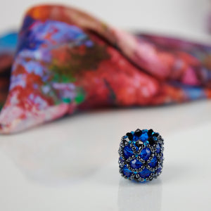 Close-up of blue handmade scarf ring, with an Orange Bouquet 100% silk Italian scarf in background.  Oksana_FineArtDesign
